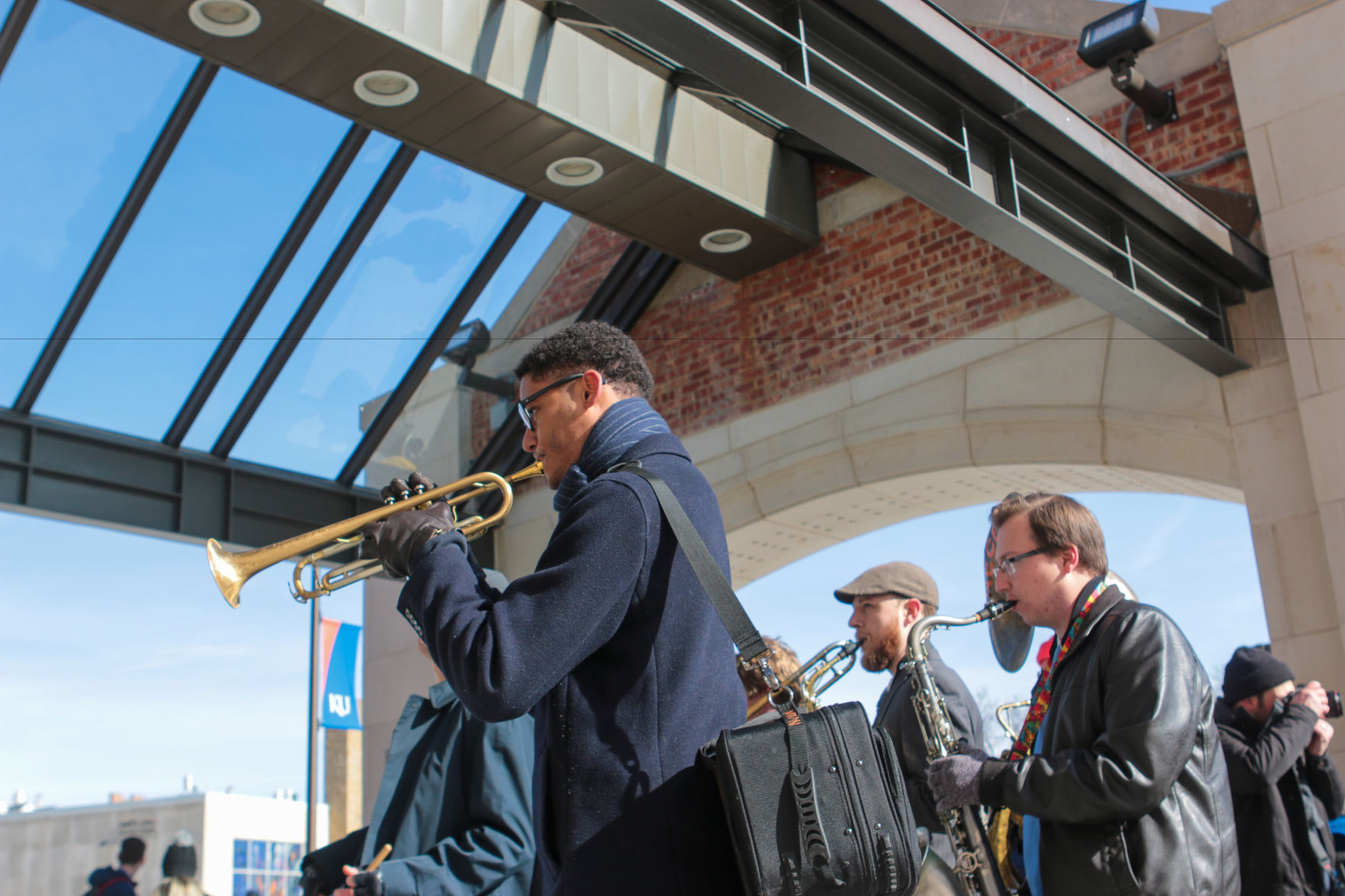 A man plays the trumpet in front of other band members under the entryway to the Kansas Union.
